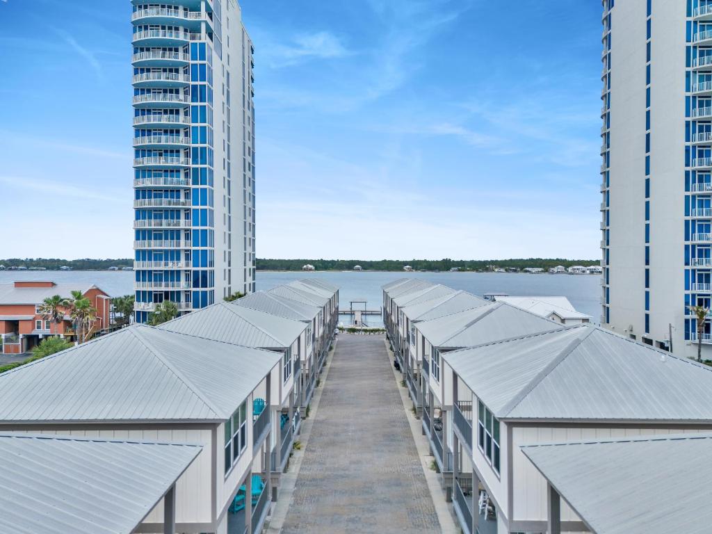 نمای هوایی از سقف‌های فلزی ردیفی خانه‌های مدرن ساحلی که در میان دو برج بلند و رو به پهنه‌ای از آب و افق قرار گرفته‌اند.