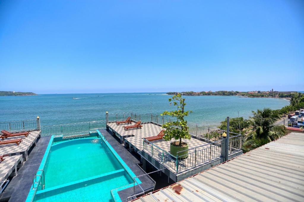 نمای باز از یک استخر کوچک روی پشت‌بام (روف‌تاپ) با کف شطرنجی، تخت‌های آفتاب‌گیر چوبی و چشم‌انداز وسیع به خلیج و اقیانوس در یک روز آفتابی. 