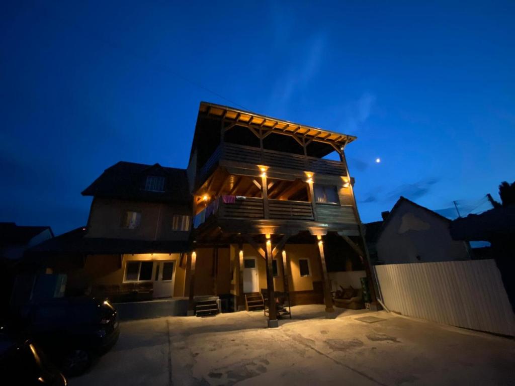 نمای بیرونی یک ساختمان اقامتی چوبی چند طبقه با تراس‌های بزرگ، نورپردازی زرد گرم در شب و محوطه پارکینگ اختصاصی زیر آسمان گرگ‌ومیش.